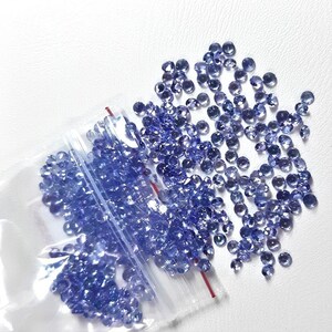 May include: A plastic bag filled with loose, round, purple gemstones. The bag is open and the gemstones are spilling out onto a white surface.