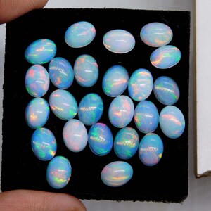 以下が含まれることがあります： 乳白色のベースに虹色の輝きを持つ、楕円形のオパールのコレクション。 オパールは黒い表面に配置され、鮮やかな光の遊びを表現しています。 宝石のサイズと色は様々です。