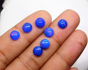 May include: A collection of seven round, vibrant blue opals. Each opal displays a play of color, with flashes of pink, green, and purple. The opals are displayed on a hand, showcasing their polished, smooth surfaces.