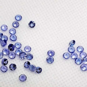 May include: A collection of small, round, light blue gemstones. The gemstones are scattered on a white surface.