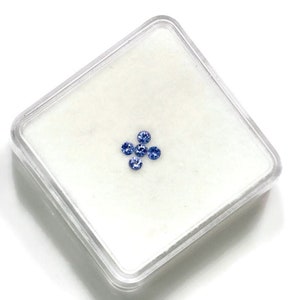 May include: Five small, round, blue gemstones in a clear plastic square container.