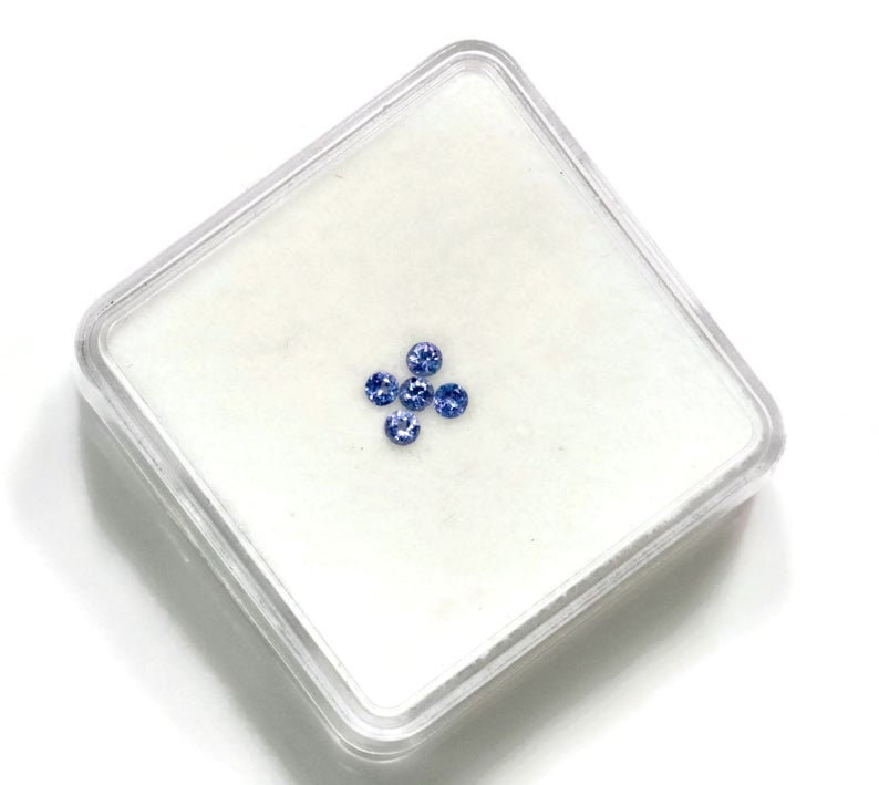 May include: Five small, round, blue gemstones in a clear plastic square container.