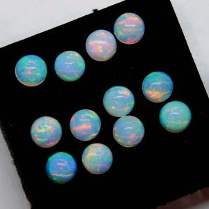 May include: A collection of eleven round opals, each displaying a play of color with iridescent flashes of blue, green, and pink. The opals are set against a black background, highlighting their vibrant hues. These gemstones are ideal for jewelry making.