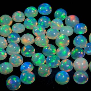 May include: A collection of round, iridescent opal cabochons in various shades of green, blue, and white. The opals are smooth and polished, with a high luster.