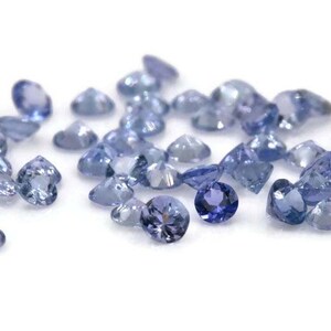 May include: A collection of loose round blue gemstones, likely Tanzanite, scattered on a white surface.