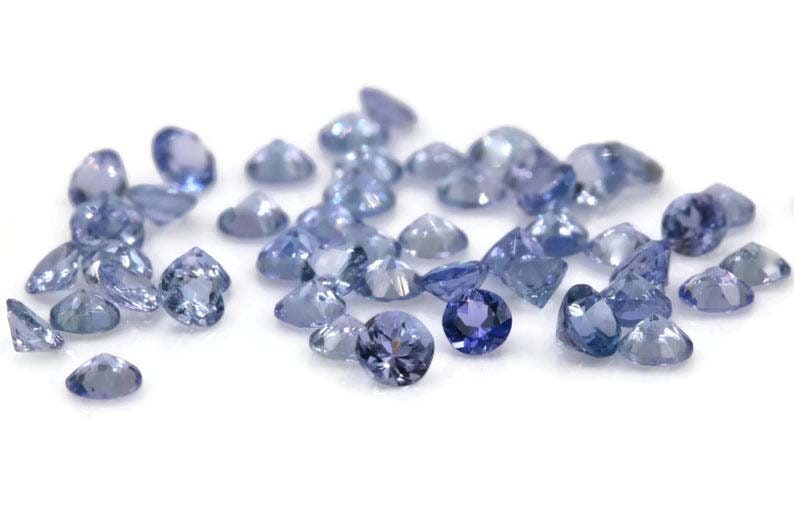 May include: A collection of loose round blue gemstones, likely Tanzanite, scattered on a white surface.