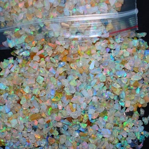 Puede incluir: Primer plano de una bolsa llena de pequeñas virutas de ópalo iridiscente. Las virutas son de varios tonos de blanco, azul, verde y naranja.