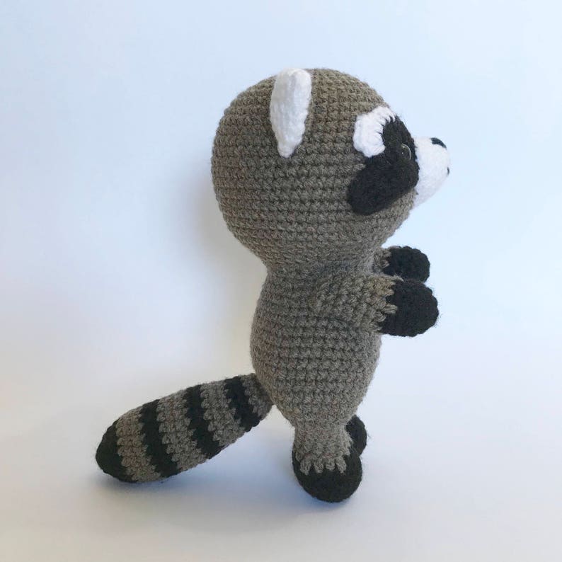 May include: A crocheted raccoon plush toy with a gray body, black and white face, and a striped tail.