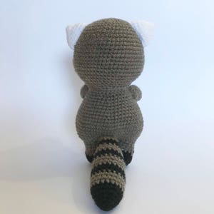 May include: A crocheted raccoon plush toy with a gray body, white ears, and a striped black and gray tail.