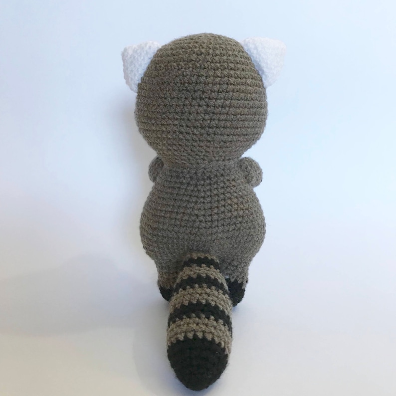May include: A crocheted raccoon plush toy with a gray body, white ears, and a striped black and gray tail.