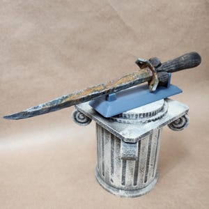 May include: A rusty, brown, and gray dagger with a wooden handle is displayed on a gray stand. The stand is on top of a white, decorative column.