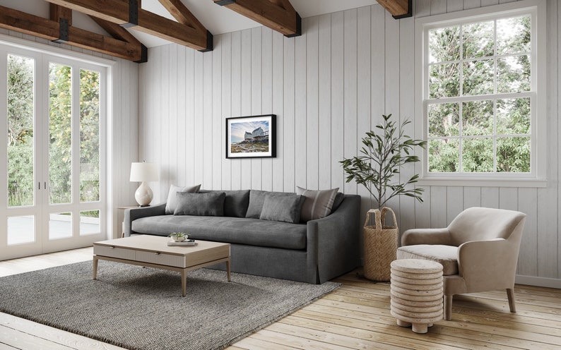 May include: A living room with a gray sofa, a coffee table, a chair, and a framed photograph on the wall. The room has a wooden floor and white walls.