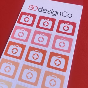 May include: Sheet of stickers featuring a first aid kit design in various shades of red, orange, and pink. The stickers have a white background and a square shape. The text "BDdesignCo" is printed at the top.