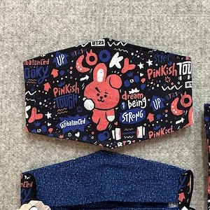 May include: Three face masks with a black background and colorful text and graphics. The text includes "Cooky", "Unbalanced", "Pinkish Tough", "BT21", and "Up". One mask is blue denim.