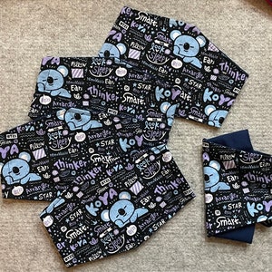 May include: Set of five black fabric face masks with a white and purple print. The print features a cartoon koala bear, stars, and the words "Thinker Smart", "Koya", "Look Sleepy", "Arranger", and "Removable Ears".