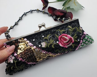 Può includere: Una pochette in satin nero con una tracolla a catena di perline. La pochette è decorata con fiori ricamati, paillettes e perline.
