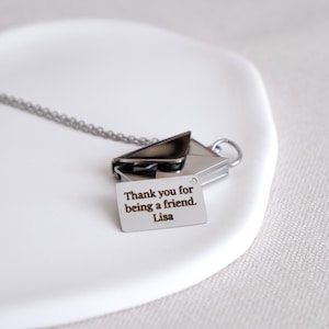 May include: A silver-toned necklace featuring an envelope pendant with a small tag. The tag is engraved with the message "Thank you for being a friend. Lisa". The necklace is displayed on a white surface.