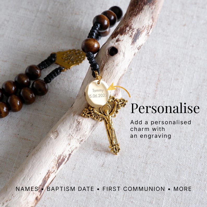 May include: A rosary with dark wooden beads and a gold-colored crucifix. A round, gold-colored charm is engraved with the name "Tommy" and the date "15.06.2022". The image includes the text "Personalise" and "Add a personalised charm with an engraving".