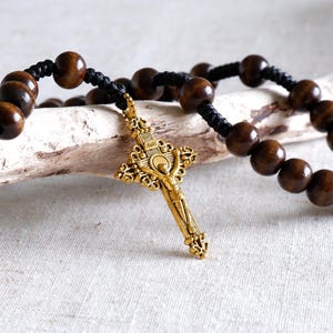 May include: A rosary with dark brown wooden beads and a gold-colored crucifix. The beads are strung on black cord. The crucifix features a detailed depiction of Jesus Christ.