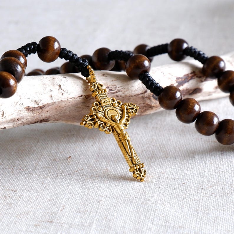 May include: A rosary with dark brown wooden beads and a gold-colored crucifix. The beads are strung on black cord. The crucifix features a detailed depiction of Jesus Christ.
