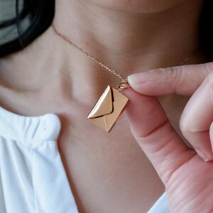May include: A rose gold necklace featuring a pendant shaped like an envelope. The pendant has a rectangular shape with a folded flap. The chain is delicate and the necklace is worn around the neck.