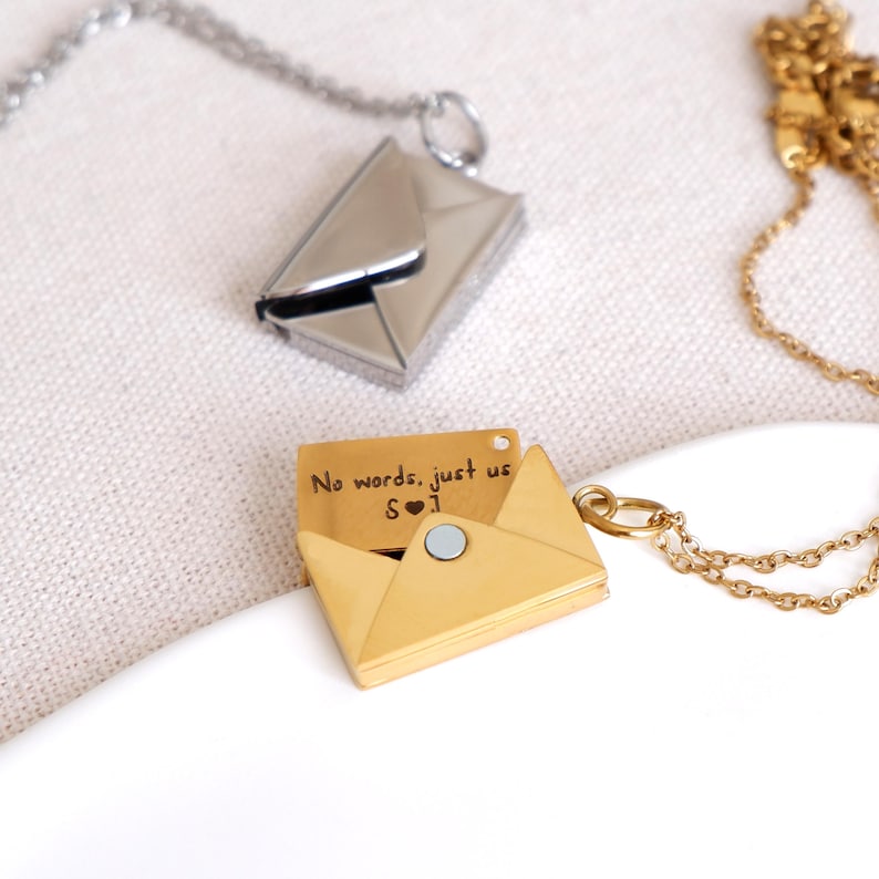 Close-up of the personalized hidden message pendant – the envelope charm is closed beside the small folded message it holds.