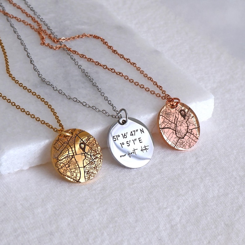 May include: Three necklaces with map pendants in gold, silver, and rose gold. One pendant has the text "51&deg; 16' 47" N 1&deg; 5' 1" E our first date". The pendants are on delicate chains, showcasing a personalized jewelry design.