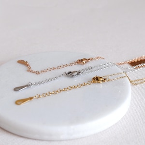 May include: Three silver chains with lobster clasps and jump rings. The chains are on a white surface.