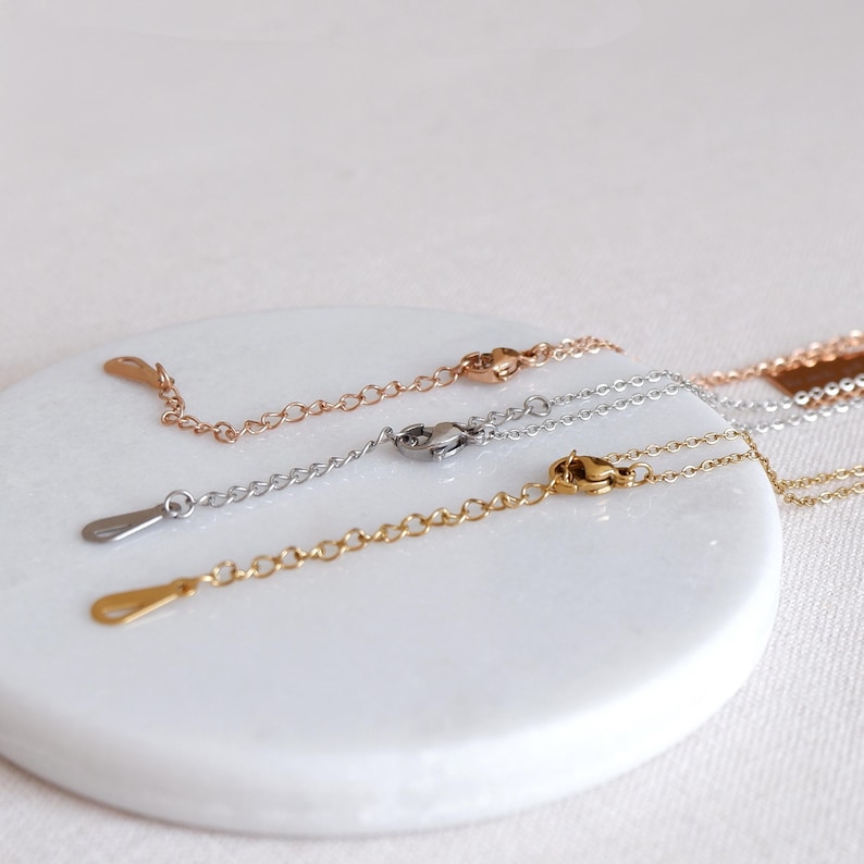 May include: Three silver chains with lobster clasps and jump rings. The chains are on a white surface.
