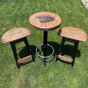 May include: A set of three wooden bar stools with black metal frames. The stools have a round, barrel-shaped seat and a footrest. The table top is round and made of wood with a black metal base. The table top has a design of a car on it.