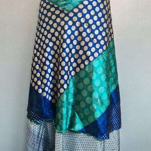 May include: A long wrap skirt featuring a patchwork design with panels of blue fabric with gold polka dots, emerald green fabric with tonal circles, and a bottom layer of light grey fabric with a small dark geometric pattern and green trim.