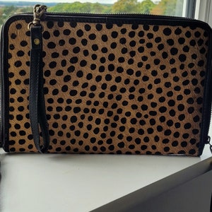 May include: A brown and black leopard print clutch with a black tassel and a gold zipper pull.