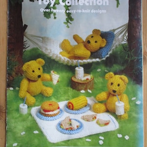 May include: A book cover featuring a yellow knitted teddy bear in a hammock with two other teddy bears having a picnic on a blanket. The book title is "Jean Greenhowe's Toy Collection" and the subtitle is "Over twenty easy-to-knit designs". The book is published by Wendy Family Choice Double Knit.