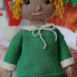 May include: Knitted elf doll wearing a green sweater, white collar, and red and white striped trousers. The elf has blonde yarn hair, brown eyes, and a rosy complexion.