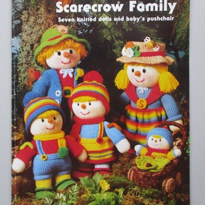 May include: A book cover featuring a colorful illustration of seven knitted scarecrow dolls, including a baby in a pushchair. The book title is "Jean Greenhowe's Scarecrow Family" and the subtitle is "Seven knitted dolls and baby's pushchair". The book cover also features the text "Double Knitting Yarn".