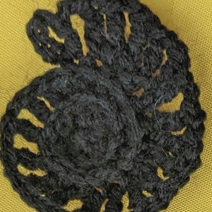 May include: A black crocheted ammonite shell on a yellow background.