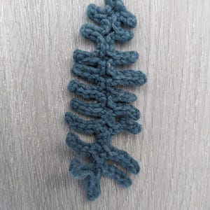 May include: A dark blue crocheted fern leaf, a handmade decorative element for a home or craft project.
