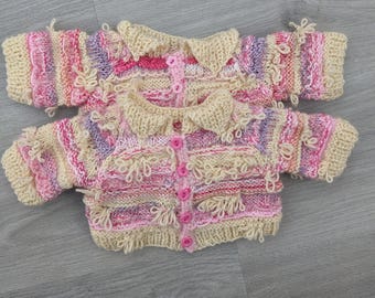 May include: Two knitted baby sweaters in pink, purple and cream with pink buttons.