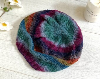 Könnte beinhalten: Eine bunte gestrickte Baskenmütze mit einem Farbmuster in Grün, Blau, Lila und Orange. Die Baskenmütze ist gefaltet und hat ein strukturiertes Strickmuster.