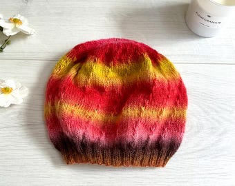 Könnte beinhalten: Eine handgestrickte Mütze mit einem Farbverlaufsmuster. Die Mütze ist rot, gelb, orange und braun.