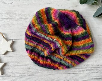 Könnte beinhalten: Eine bunte, handgestrickte Beanie-Mütze. Die Mütze hat horizontale Streifen in Lila, Pink, Orange, Gelb und Grün. Sie ist aus weichem Garn gefertigt und für kaltes Wetter geeignet. Ein handgefertigter Artikel.