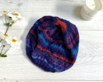Könnte beinhalten: Eine gestrickte Mütze in den Farben Blau, Rot und Lila.