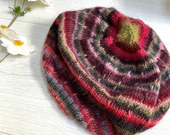 Könnte beinhalten: Eine bunte gestreifte Strickmütze mit einem Farbmuster in Rot, Rosa, Grün und Schwarz. Die Mütze ist aus weichem Garn gefertigt und hat eine leicht lockere Passform.