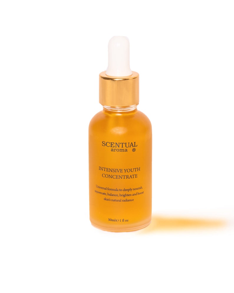 May include: A glass bottle with a gold cap and a white dropper top. The bottle is filled with a yellow liquid and has a label that reads "SCENTUAL aroma INTENSIVE YOUTH CONCENTRATE Universal formula to deeply nourish, rejuvenate, balance, brighten and boost skin's natural radiance 30ml e 1 fl oz".