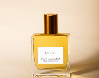 Könnte beinhalten: Eine durchsichtige Glasflasche mit goldfarbenem Verschluss und einem Etikett mit der Aufschrift "LE SOLDE SCENTUAL AROMA* BOTANICAL PERFUME OIL".