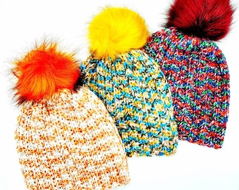 May include: Three knitted winter hats with colorful pom poms. The hats are in orange, yellow, and blue with white stripes. The pom poms are made of faux fur.