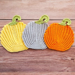 May include: Three crocheted pumpkins in yellow, gray, and orange. The pumpkins are arranged in a row on a wooden surface.