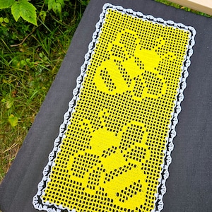 May include: A yellow crocheted table runner with a white crocheted border. The runner has a floral design.