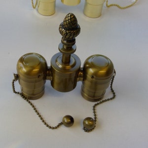 May include: A brass ceiling fan light kit with two sockets and a decorative acorn finial. The kit includes two pull chains with decorative ball ends.