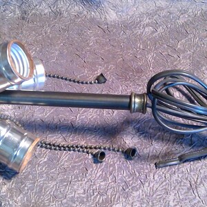 May include: A black metal light fixture with three sockets and a black cord. The fixture has a swiveling head and is designed for hanging.